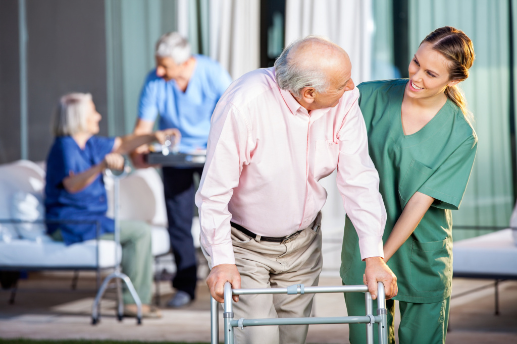 Caretaker helping senior gentleman walk with zimmer frame
