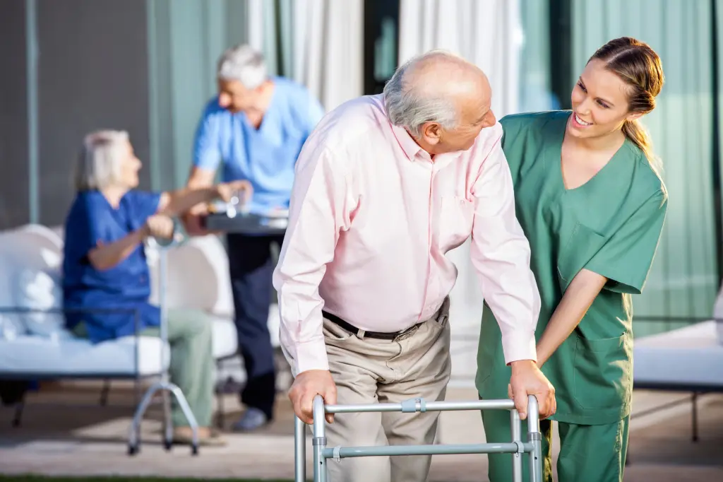 Caretaker helping senior gentleman walk with zimmer frame